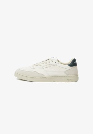 Beige leather sneakers with suede accents, flat laces, a prominent rubber sole, and a dark green heel detail; minimalist design.
