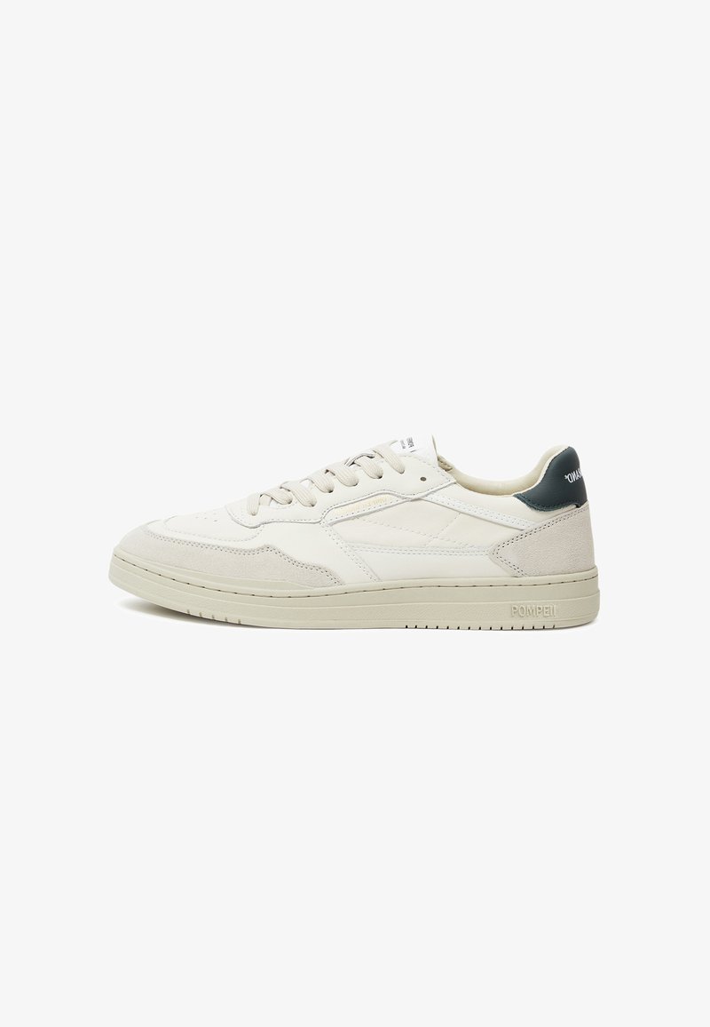 Beige leather sneakers with suede accents, flat laces, a prominent rubber sole, and a dark green heel detail; minimalist design.
