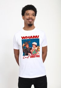 Bílý tričko se zajímavým barevným potiskem s nápisy "WHAM!" a "Last Christmas". Design obsahuje dvě postavy v zimním oblečení s vánočními akcenty.