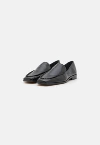 Mocassins en cuir noir avec une finition lisse, bout pointu, couture tissée décorative et un petit talon rectangulaire.