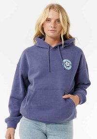 Lilla fleece hoodie med kængurulomme, snoretræk i hætten og grafisk logo detalje på brystet, som er parret med lyseblå jeans.