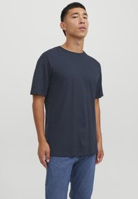 Marineblå bomull T-skjorte, korte ermer, rund hals, avslappet passform. Brukt med lyseblå denimjeans, glatt tekstur, minimalistisk design.