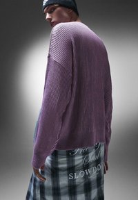 Maglione viola a coste con una vestibilità ampia, texture leggera e maniche lunghe, abbinato a una gonna a quadri bianca e nera.