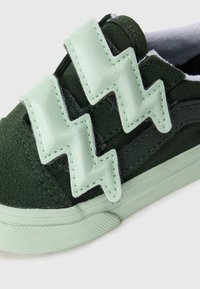 Baskets en toile vertes avec une surface texturée, présentant deux bandes zigzag vert menthe sur le dessus. La semelle est d'un vert menthe clair.