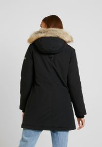 Black parka jacket with a fur-trimmed hood, featuring a cinched waist, long sleeves, and a smooth texture. Notable hardware at the collar.