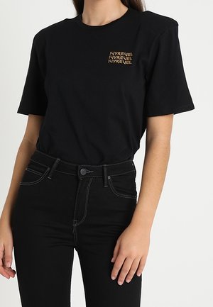 Black cotton t-shirt with short sleeves featuring a small gold graphic on the left chest. Paired with high-waisted black jeans.