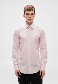 Ροζ ανοιχτό ροζ πουκάμισο με μακρύ μανίκι κατασκευασμένο από βαμβακερό ύφασμα, με κλασικό γιακά, κούμπωμα μπροστά με κουμπιά και ίσια γραμμή. Ομαλή υφή.