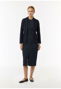 Czarna dżinsowa marynarka i dopasowana sukienka midi z przodu rozcięciem, o dopasowanym kroju i minimalistycznym designie. Czarne baleriny dopełniają całość.