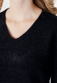 Pulover cu guler în V, de culoare albastru închis, realizat dintr-un material moale și texturat. Prezintă cusături delicate și un aspect ușor pufos.