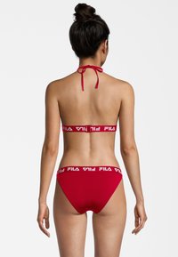 Bikini rosso con collare a halter e spallina sul retro con branding bianco "FILA". L'insieme include uno slip a vita bassa abbinato con dettaglio del logo.