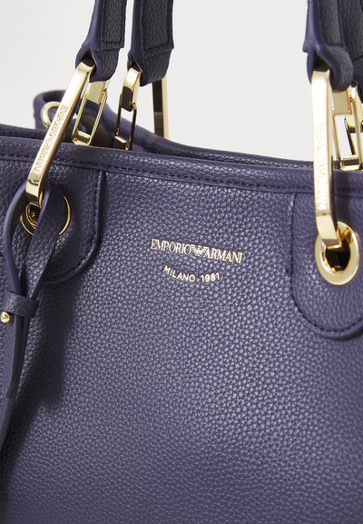 Navy textured handbag featuring gold hardware, with "EMPORIO ARMANI" and "MILANO 1981" embossed on the front.