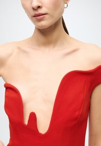 Red dress with a deep V-neckline and off-shoulder design. Smooth fabric with a slight sheen and cutout detail at the front neckline.