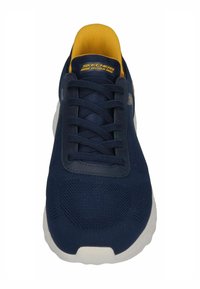 Scarpa da ginnastica blu navy con tomaia in rete texturizzata, colletto in tessuto giallo e suola in gomma bianca. Presenta un tradizionale design con lacci.