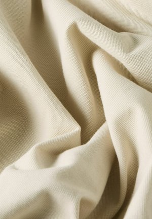 Crèmekleurige textuurstof met zachte plooien en een wafelgebreid patroon dat licht- en schaduwcontrasten creëert.