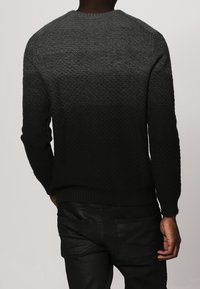Maglione lavorato a maglia grigio scuro con un motivo testurizzato, con polsini e orlo a costine e un collo rotondo. Indossato con pantaloni neri.