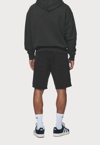 Felpa nera con cappuccio, abbinata a pantaloncini di jeans neri con tasche posteriori. Indossata con calzini bianchi e scarpe da ginnastica nere.