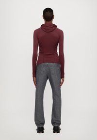 Vínová mikina s dlouhými rukávy a kapucí, kombinovaná s volnými šedými džíny. Oblečení má hladkou texturu a minimalistický design. Černé boty dokončují vzhled.