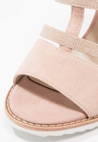 Sandale en daim rose clair à bout ouvert avec une large bride avant et une bride de cheville plus fine et texturée sur semelle blanche.