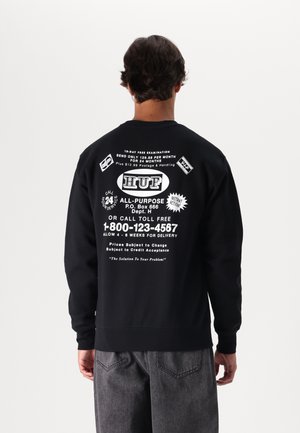 Sudadera negra con texto gráfico y logotipos en blanco en la parte posterior. Manga larga con puños y dobladillo acanalados. Diseño sencillo y corte relajado.