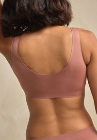 Hele-roosa, veniv kangasest spordirinnahoidja laiade rihmade ja ümmarguse seljaga disainiga, millel on sile tekstuur ja lihtne lõige.