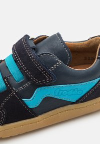 Sneaker in pelle scamosciata nera e pelle blu navy con dettagli turchesi, chiusura in velcro, cuciture a contrasto e suola in gomma marrone.