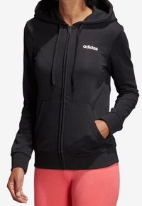 Sweat à capuche noir zippé avec cordons, doté d'une poche avant et du logo Adidas blanc sur le côté gauche de la poitrine. Tissu doux avec une texture lisse.