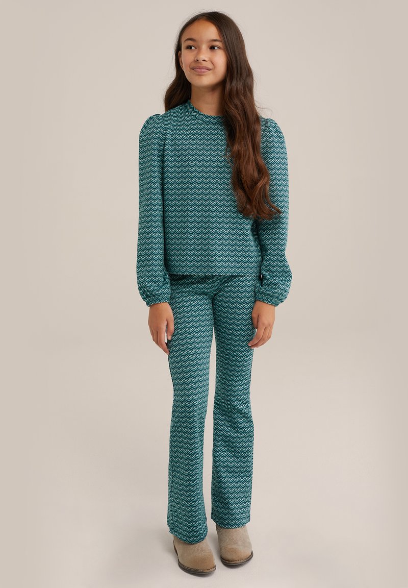 Tyrkysový dvoudílný outfit s vlnitými vzory. Halenka s dlouhými rukávy a nabíranými rameny a kalhoty do zvonu. Tkanina má hladkou texturu.