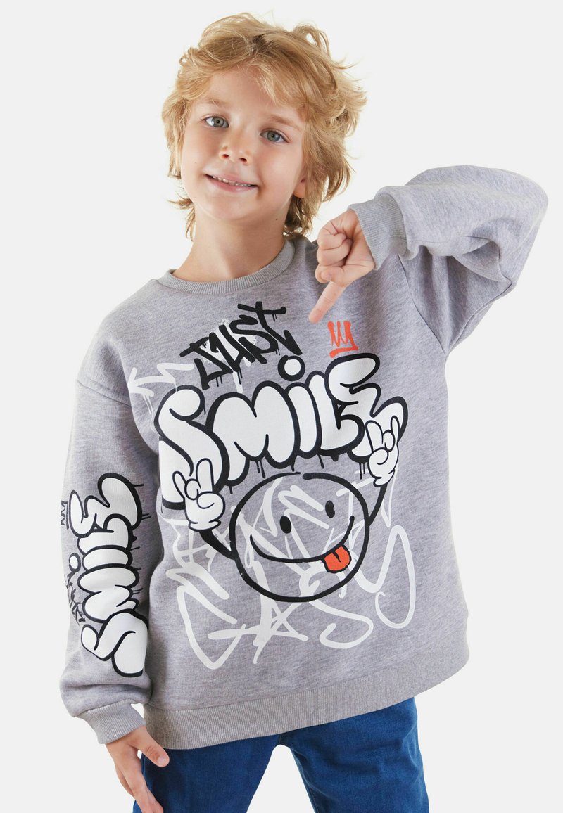 Grijze sweatshirt met speelse grafische ontwerpen in zwart-wit, met een glimlachend gezicht en kleurrijke tekst. Zachte textuur, relaxte pasvorm.