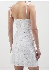 Robe blanche avec un motif floral en œillets, corsage ajusté, fines bretelles nouées aux épaules, texture lisse et longueur au-dessus du genou.