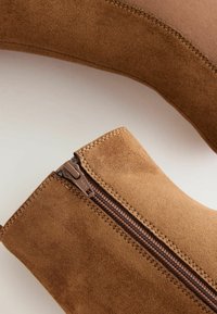 Bruna mocka ankelstövlar med en sidodragkedja, med en slät textur, sydda detaljer och en smidig, avsmalnande design.