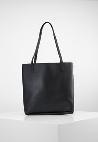 Czarna skórzana torba typu tote z dwoma długimi paskami, nieregularnym kształtem i gładką teksturą. Prosty design bez widocznych elementów metalowych ani ozdób.