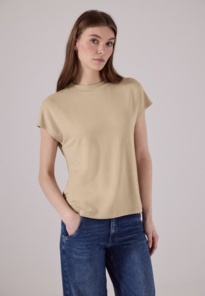 Beige kortærmet t-shirt med rund halsudskæring, blød tekstur og afslappet pasform, parret med blå denim jeans. Enkel og minimalistisk design.
