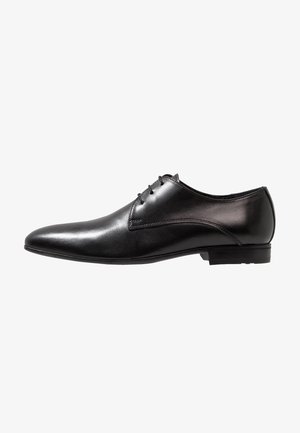Chaussure habillée en cuir noir avec un bout pointu, une texture lisse et trois œillets pour les lacets. Design minimaliste avec une semelle plate.