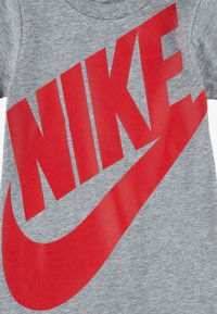 Grå t-skjorte laget av bomull med en stor rød "NIKE"-logo og en swoosh-grafikk som er tydelig vist over fronten.