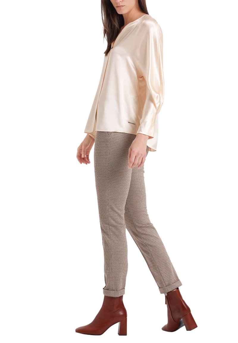 Blouse en satin crème avec un col en V, associée à un pantalon marron à carreaux et des bottines marron à talons. Texture lisse et coupe décontractée.