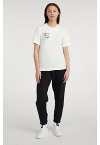 Bílý tričko s černým nápisem "Ženy vlny", spárované s černými tepláky a bílými teniskami. Jednoduchý, neformální design.