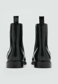 Bottines en cuir noir avec panneaux élastiques sur les côtés, bouts ronds, semelles plates et languettes à l'arrière, présentant une finition brillante.