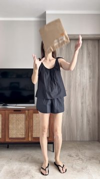 Femme en haut sans manches noir et shorts lançant un sac en papier brun à l'intérieur près d'une télévision et d'un meuble en bois.
