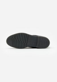 Suela de zapato de goma negra con un patrón texturizado, que presenta múltiples ranuras horizontales para tracción y una impresión de logo.