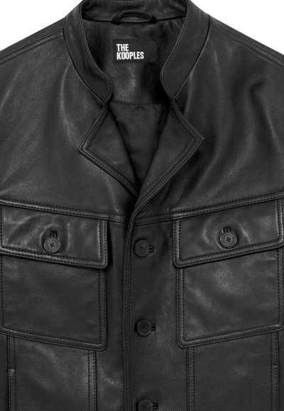Chaqueta de cuero negra con cuello alzado, dos bolsillos delanteros y cierres de botón. Presenta una textura suave y un diseño clásico.