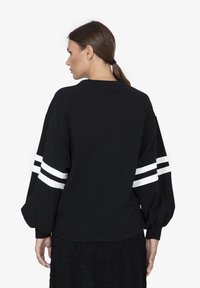 Felpa nera con una vestibilità rilassata e maniche lunghe e gonfie. Presenta strisce bianche sulle maniche e un colletto rotondo. Tessuto in cotone morbido.