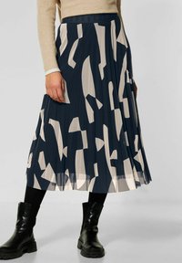 Gonna midi plissettata in navy con forme astratte beige. Realizzata in tessuto leggero, presenta una vita aderente e una finitura testurizzata.