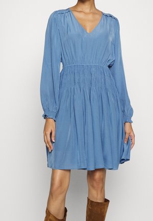 Blauwe jurk met lange mouwen, een V-hals, een gesmokte taille en geplooide details, gemaakt van soepele stof, die tot halverwege de dij komt, gecombineerd met bruine laarzen.