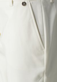 White trousers made of smooth fabric featuring a side pocket, a metal button, and clean stitching, emphasizing a tailored appearance.