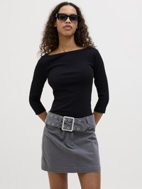 Black ribbed long-sleeve top with an off-shoulder design paired with a gray mini skirt featuring a wide belt with grommets and a large buckle.