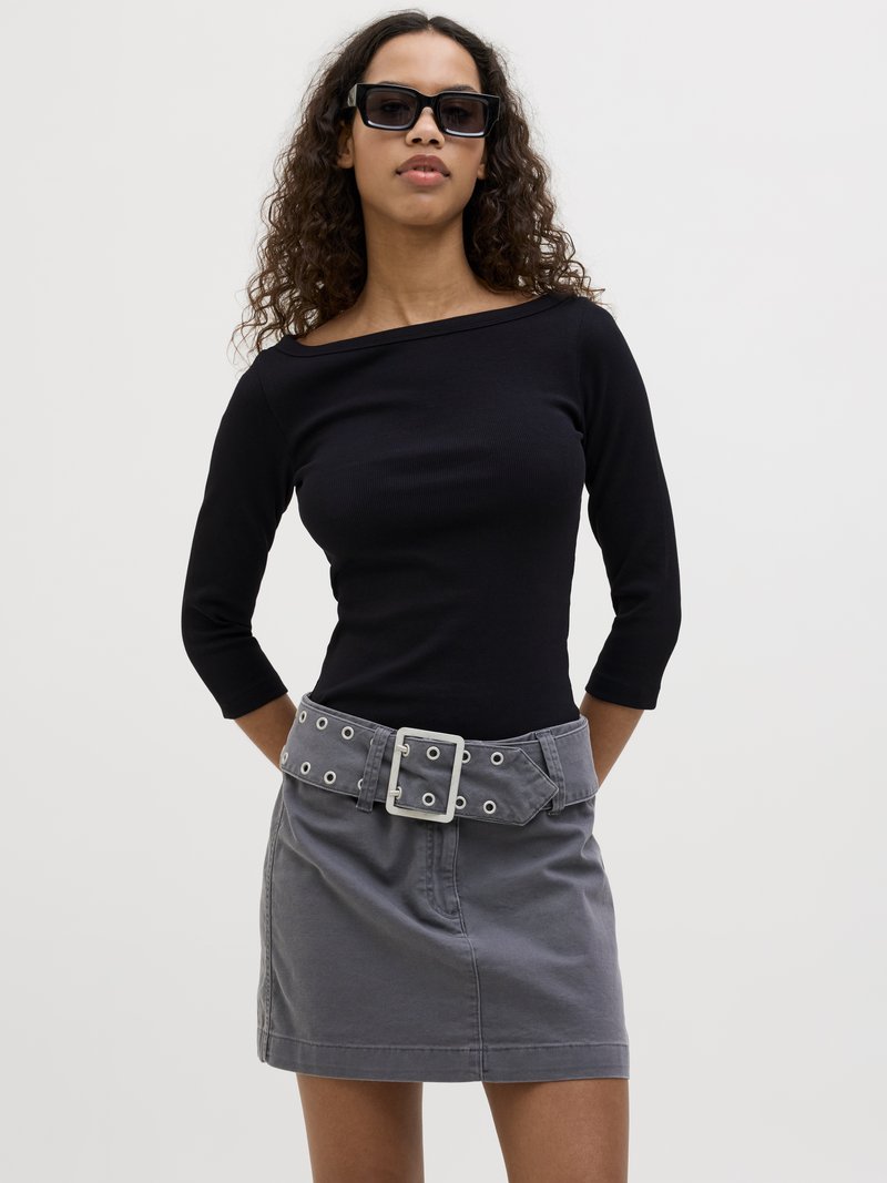 Black ribbed long-sleeve top with an off-shoulder design paired with a gray mini skirt featuring a wide belt with grommets and a large buckle.