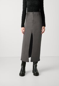 Grå denim maxi-skirt med en frontal split, høy midje og subtile sømdetaljer, kombinert med svarte plattform ankelboots.