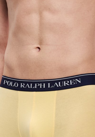 Žlté boxerky s námorníckym modrým pásom, na ktorom je bielym textom "POLO RALPH LAUREN". Materiál je hladký s priliehavým strihom.
