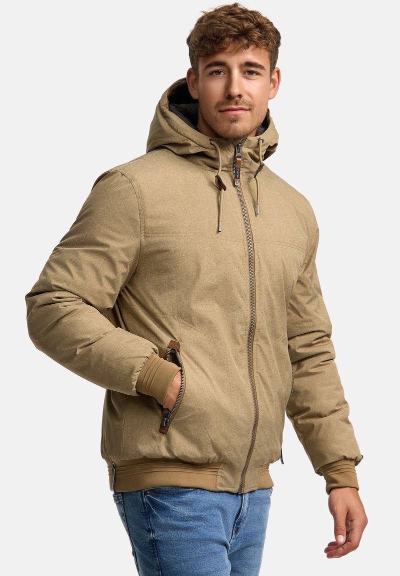 Beige pufferjakke med hætte, lynlåslukning, sidelommer og ribbede manchetter. Har en tekstureret overflade og justerbare snore.