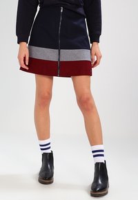 Falda corta en línea A con cremallera frontal, que presenta colores en bloque: marino, gris y burdeos. Combinada con botas chelsea negras y calcetines a rayas.